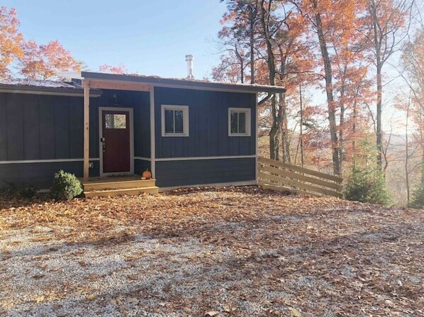 A two-story cabin with a dark exterior, a red door, and a small porch.