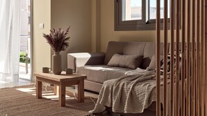 A living room with a sofa, a coffee table, a vase with dried plants, and a window with blinds. - Laura Suites (Zakynthos)