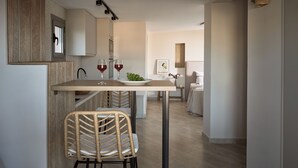 A modern kitchen with a dining area, featuring a wooden ceiling, a light-colored floor, and a view into the adjacent bedroom. - Laura Suites (Zakynthos)
