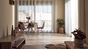 A modern living room with a dining area, large windows with sheer curtains, and a view of buildings outside. - Laura Suites (Zakynthos)