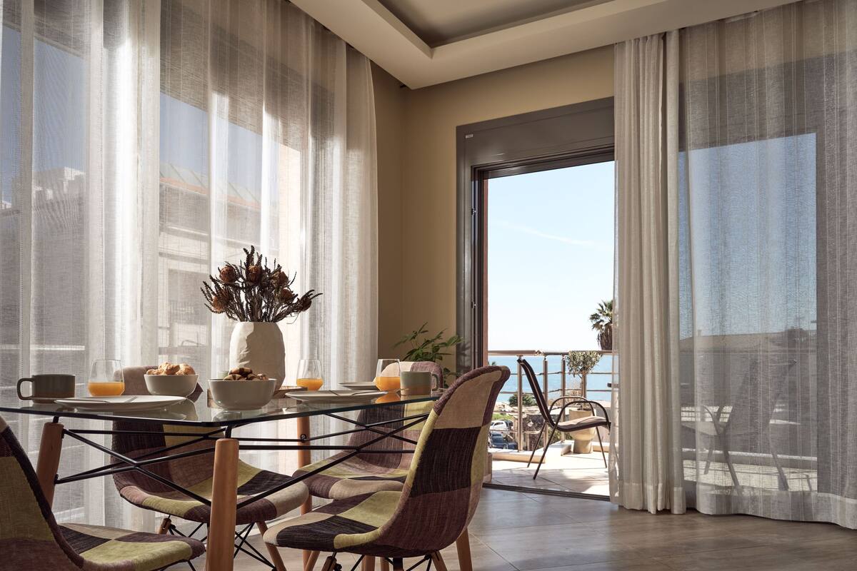 A dining area with a glass table, chairs, and a view of the sea through large windows.