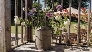 A rustic outdoor area with a metal pot containing flowers, wooden deck, and a wooden fence. - Spindleberry Hut (Dorchester)