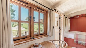 A room with a wooden window, a bed with a checkered blanket, a round wooden table with coasters, and a chair. - Spindleberry Hut (Dorchester)