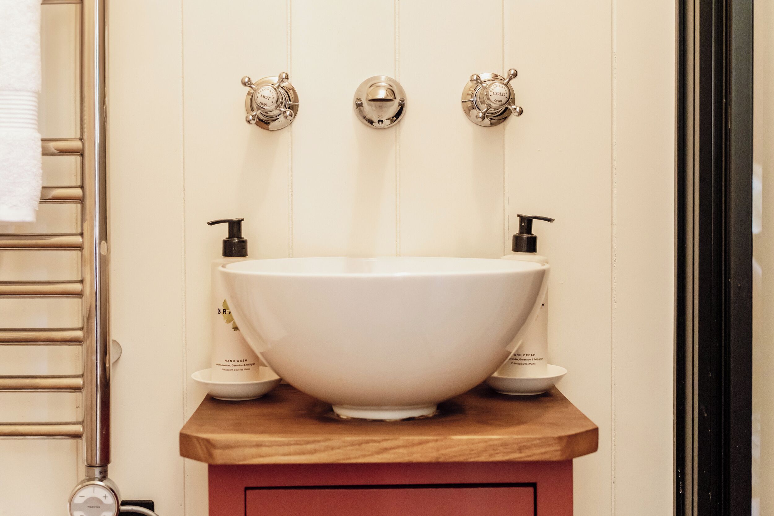 Un baño con un lavamanos blanco tipo recipiente, encimera de madera y dos grifos instalados en la pared.