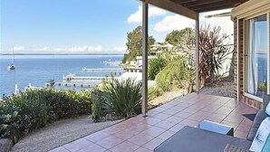 A covered patio with a view of the sea, a dock, and a building with a garden. - Sparkling Waters - Jetty & Games Room! (Rathmines)