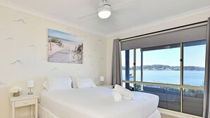 A hotel room with a bed, a nightstand, a painting, and a large window with a view of the sea. - Sparkling Waters - Jetty & Games Room! (Rathmines)