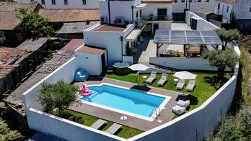 Una piscina en la azotea con sillones de descanso y sombrillas, rodeada por un muro blanco y follaje.