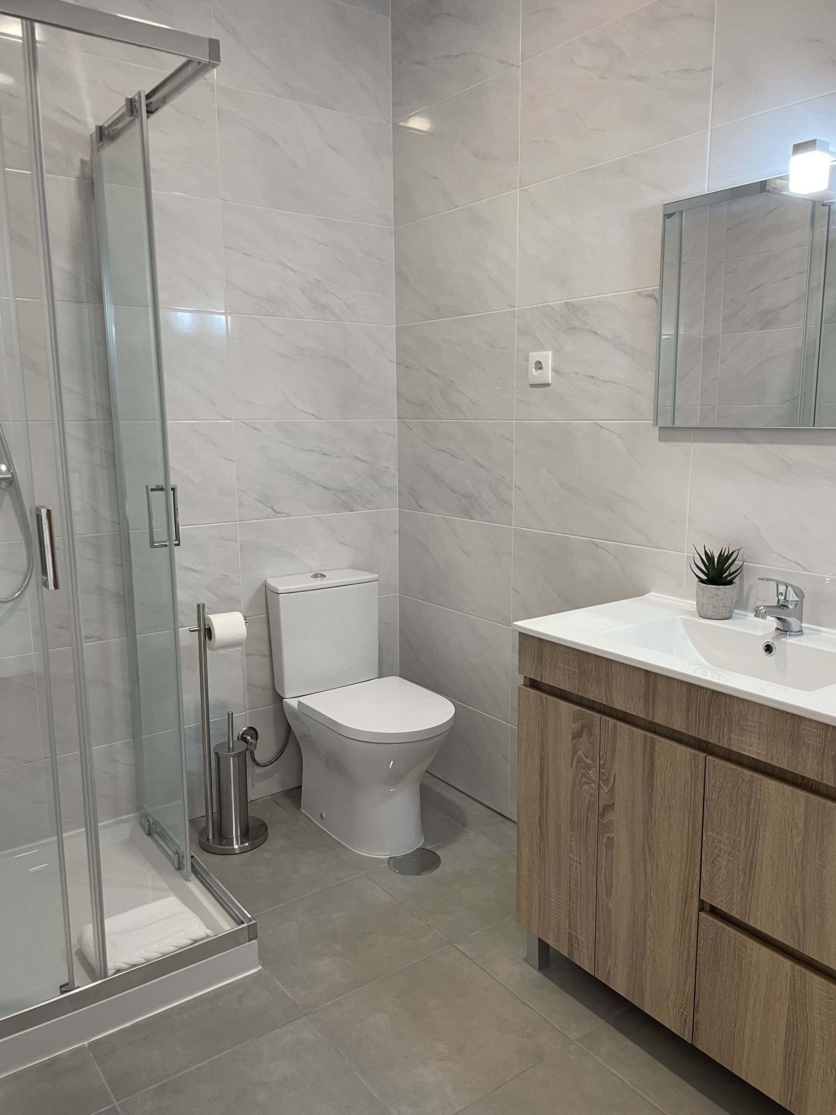 Un baño moderno con cabina de ducha de vidrio, inodoro y lavabo con armario de madera.