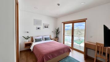 Un dormitorio moderno con cama, mesitas de noche, un escritorio y un balcón con sillas.