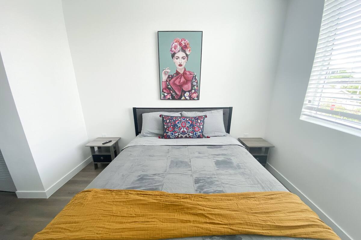 Un dormitorio con cama, mesita de noche y ventana con persianas.