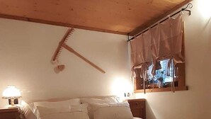 A bedroom with a wooden ceiling, a bed with white linens, a bedside table with a lamp, and a window with curtains. - Chalet-Tabia'al Sol romantic apartment with breathtaking views in the Dolomites (Pecol)