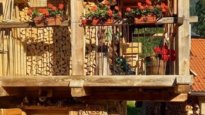 A rustic wooden building with a balcony adorned with red flowers, a stone entrance, and a small outdoor seating area with a table and chairs. - Chalet-Tabia'al Sol romantic apartment with breathtaking views in the Dolomites (Pecol)