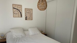 Quarto com cama grande, duas pinturas abstratas penduradas na parede, luminária pendente trançada e abajures.