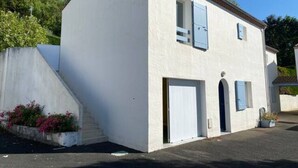 Um edifício de dois andares com fachada branca, uma pequena janela com venezianas azuis e uma porta de garagem.
