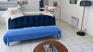 Um sofá azul com almofadas combinando, uma mesa de centro de madeira com uma revista e um abajur.