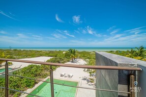 Un balcón con vista a una playa, una piscina y una zona de arena con sillones de descanso.