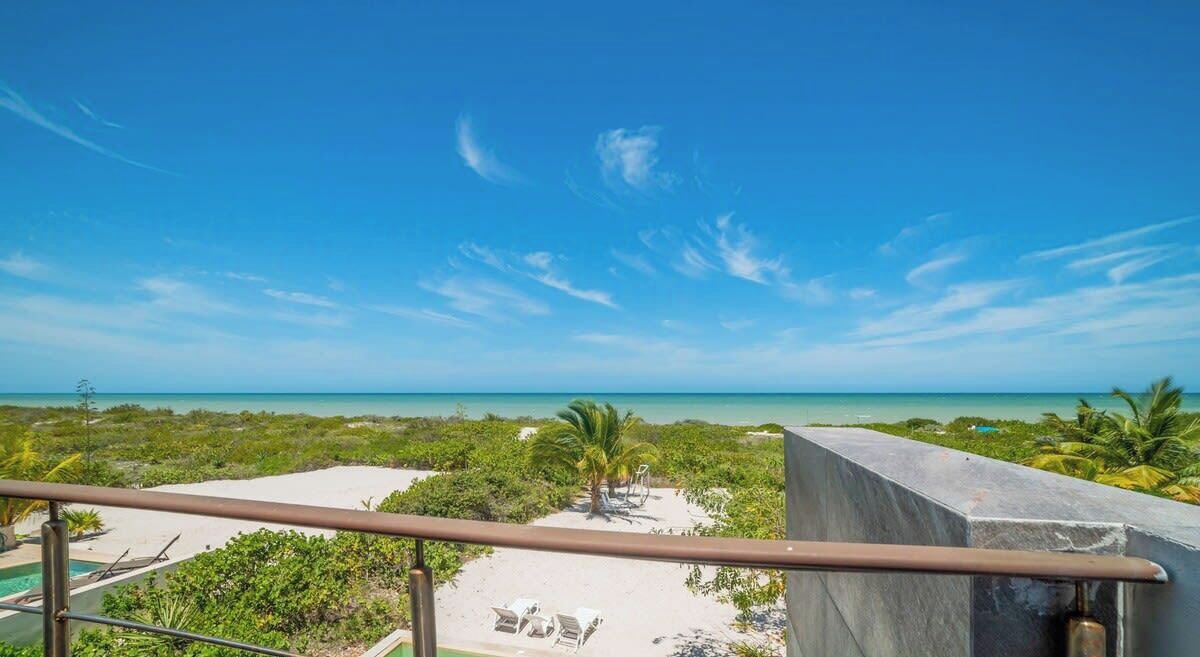 A balcony with a view of a beach, palm trees, and a clear sky.