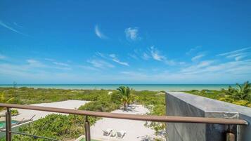 A balcony with a view of a beach, palm trees, and a clear sky.