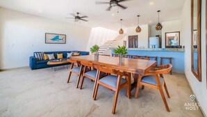 A spacious living area with a wooden dining table, blue sofa, ceiling fans, and a staircase leading to an upper level. - Luxe Beachfront Villa, Private Pool & Beach Access (Progreso)