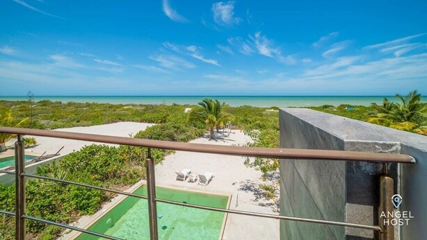 A balcony with a view of a beach, a pool, and a sandy area with lounge chairs. - Luxe Beachfront Villa, Private Pool & Beach Access (Progreso)