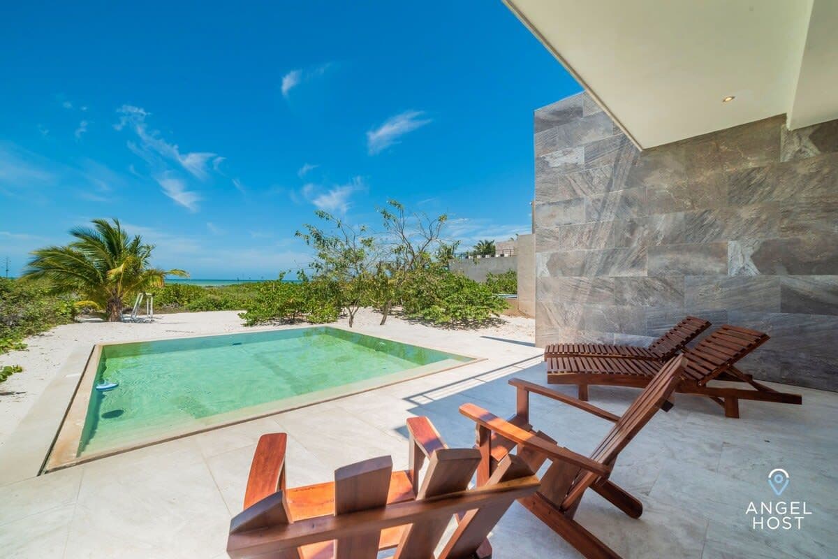 A poolside area with a view of the ocean, a stone wall, and wooden lounge chairs.