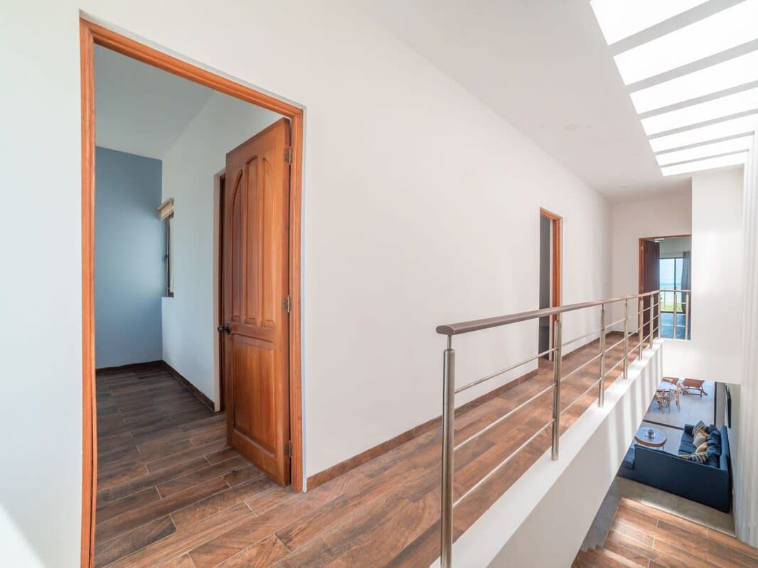 A modern interior with a wooden door, a staircase with metal railings, and a view of a living area with a sofa and a table.