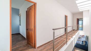 A modern interior with a wooden door, a staircase with metal railings, and a view of a living area with a sofa and a table.