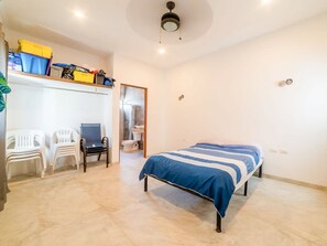 Un dormitorio con cama, escritorio y silla. Hay cajas de almacenamiento en la pared y un ventilador de techo.