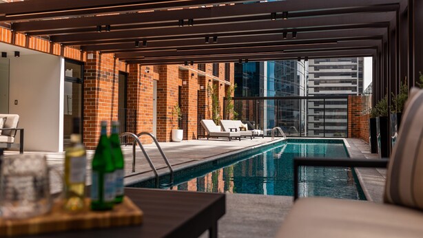 Un área de piscina exterior moderna con sillones reclinables y un muro de ladrillo.