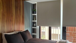 Un dormitorio con cama, techo de listones de madera, ventana y repisa con objetos decorativos.