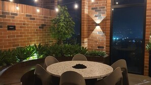 Un área de estar al aire libre con una mesa redonda y sillas, rodeada de muros de ladrillo y plantas en macetas.