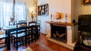 Una sala de estar acogedora con chimenea, vigas de madera y un comedor con sillas y una mesa.