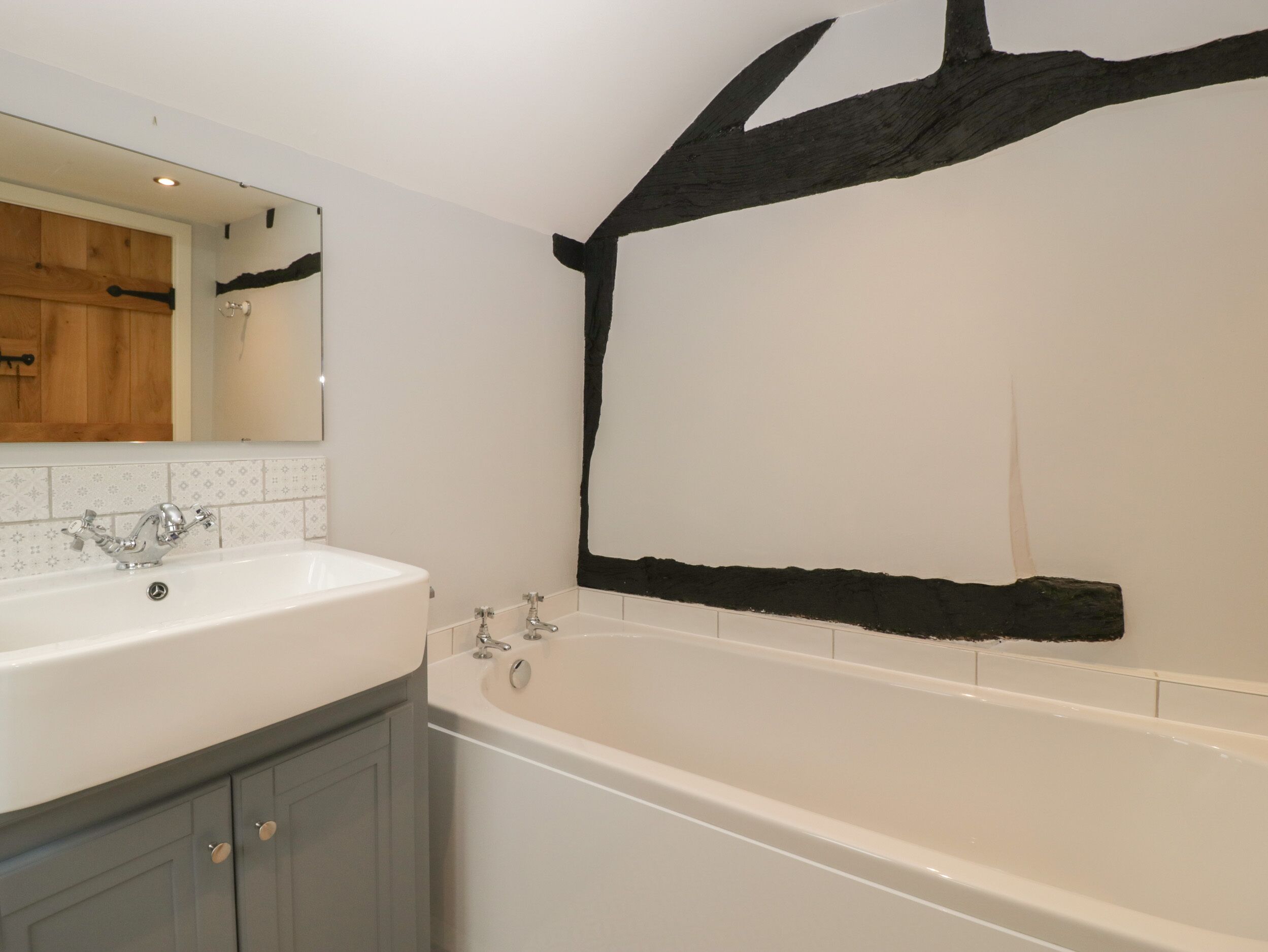 A bathroom with a white sink, a mirror, a bathtub, and a wooden beam on the wall.