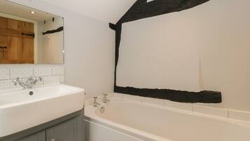 A bathroom with a white sink, a mirror, a bathtub, and a wooden beam on the wall.