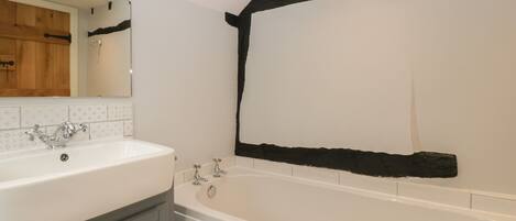 A bathroom with a white sink, a mirror, a bathtub, and a wooden beam on the wall.