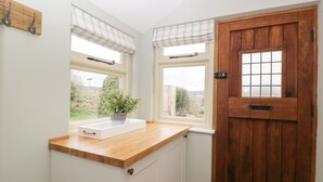 Una cocina con encimera de madera, dos ventanas con persianas, una puerta con diseño de cuadrícula y un armario blanco.