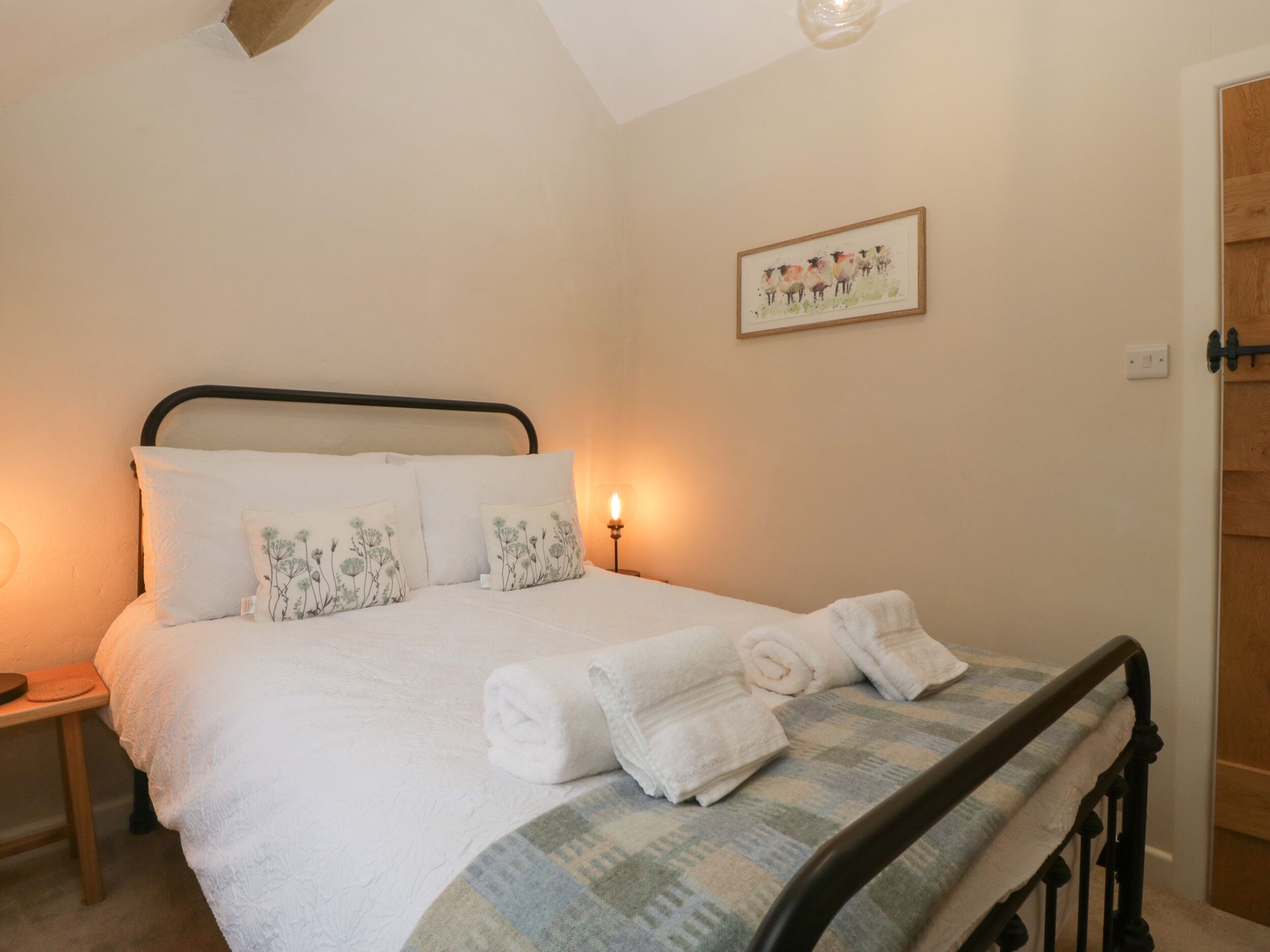 Un lit bien fait, avec du linge de lit blanc et des coussins décoratifs, une table de chevet avec une lampe et un tableau encadré au mur.