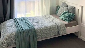Une chambre à coucher avec un lit, une fenêtre avec des rideaux et une vue sur les bâtiments à l’extérieur.