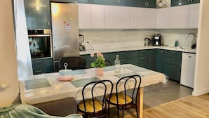 Une cuisine compacte avec un coin repas, comprenant un réfrigérateur, un four, une machine à café et une petite table avec des chaises.