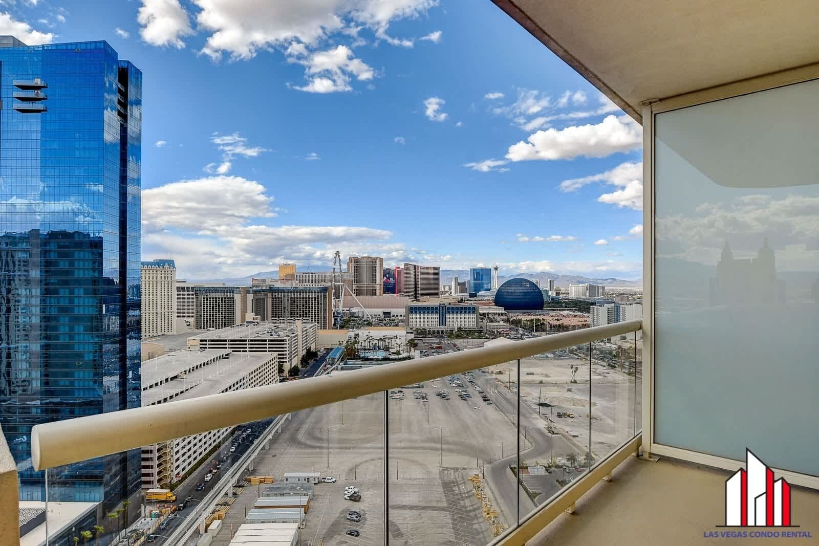 A cityscape with modern buildings, including a distinctive dome-shaped structure, viewed from a balcony with a clear sky.