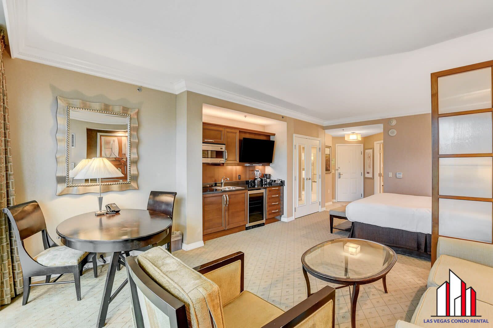A hotel room with a dining area, kitchenette, and a bed.