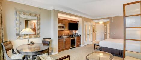 A hotel room with a dining area, kitchenette, and a bed.