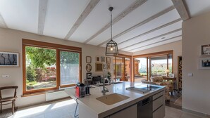 Una cocina amplia con una isla grande, un comedor con mesa y sillas, y vistas al jardín a través de ventanas amplias.