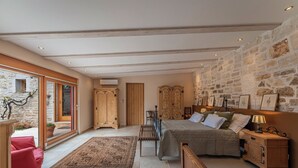 Un dormitorio con pared de piedra, muebles de madera, una cama con almohadas, un banco y vistas a través de un ventanal.