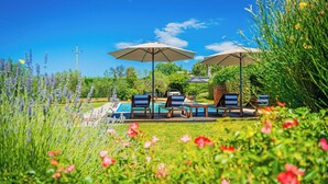 Zona de piscina con sillones de descanso y sombrillas, rodeada de exuberante vegetación y flores.