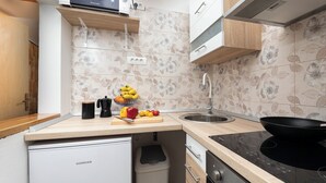 Eine kleine Küche mit einem Koncar-Kühlschrank, einer Holz Arbeitsplatte, einem schwarzen Herd und einem Spülbecken.
