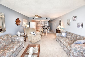 Relax in this inviting living room with a sofa, armchair, and coffee table, surrounded by artwork and a decorative mirror.