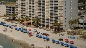 A multi-story hotel with balconies, a beach with umbrellas, and a clear sky. - 0112 Waters Edge Resort 3 Bedroom Condo by RedAwning (Murrells Inlet)