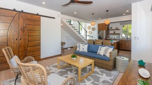 A modern living room with a sofa, chairs, a coffee table, and a kitchen in the background. - Casa Coral And Casa Palmera 4 Bedroom Home by RedAwning (Roatan)