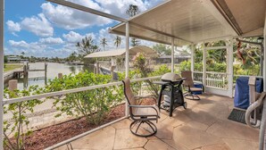A covered patio with a view of a lake, outdoor furniture, and a grill.